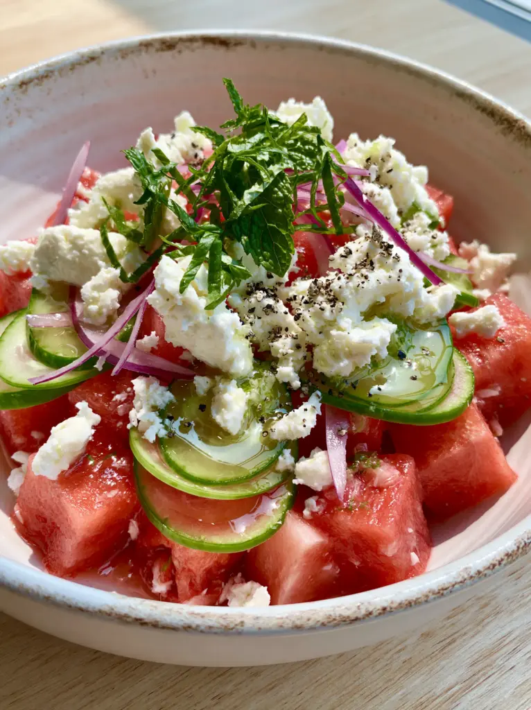 Close-up of crispy Persian cucumber half-moons and creamy Greek feta crumbles in a watermelon salad.