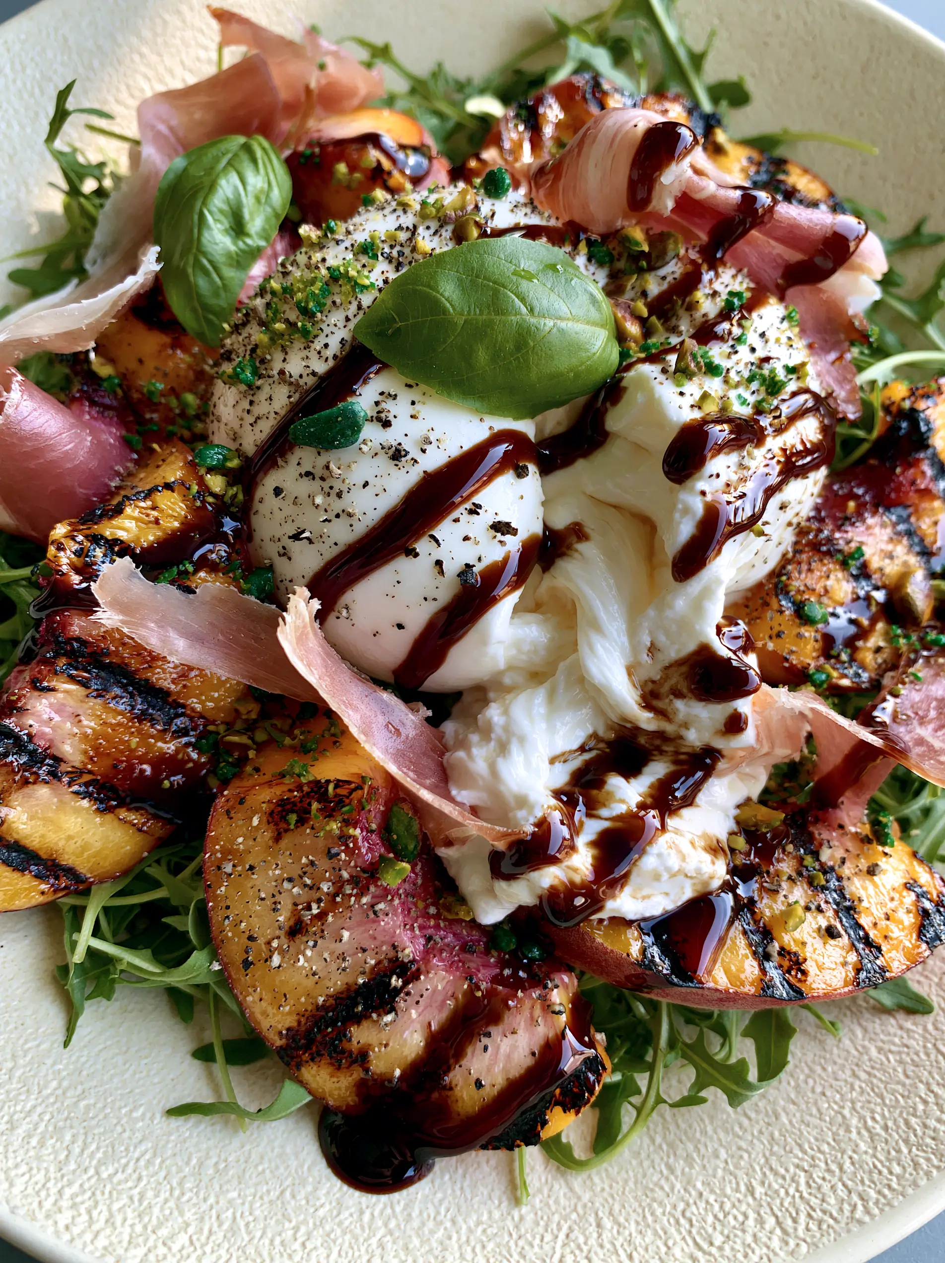 Close-up of a Grilled peach salad showing the glossy balsamic glaze clinging to caramelized peach wedges and the flowing creamy center of fresh burrata.