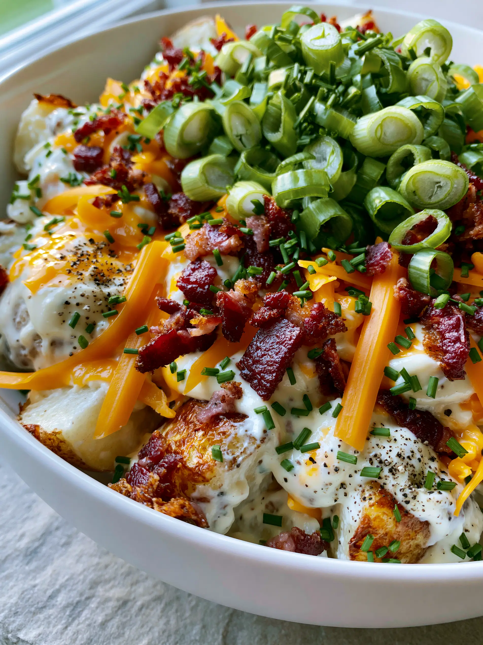 High-angle smartphone photo of loaded potato salad showing golden-brown roasted potato edges and melting orange cheddar.