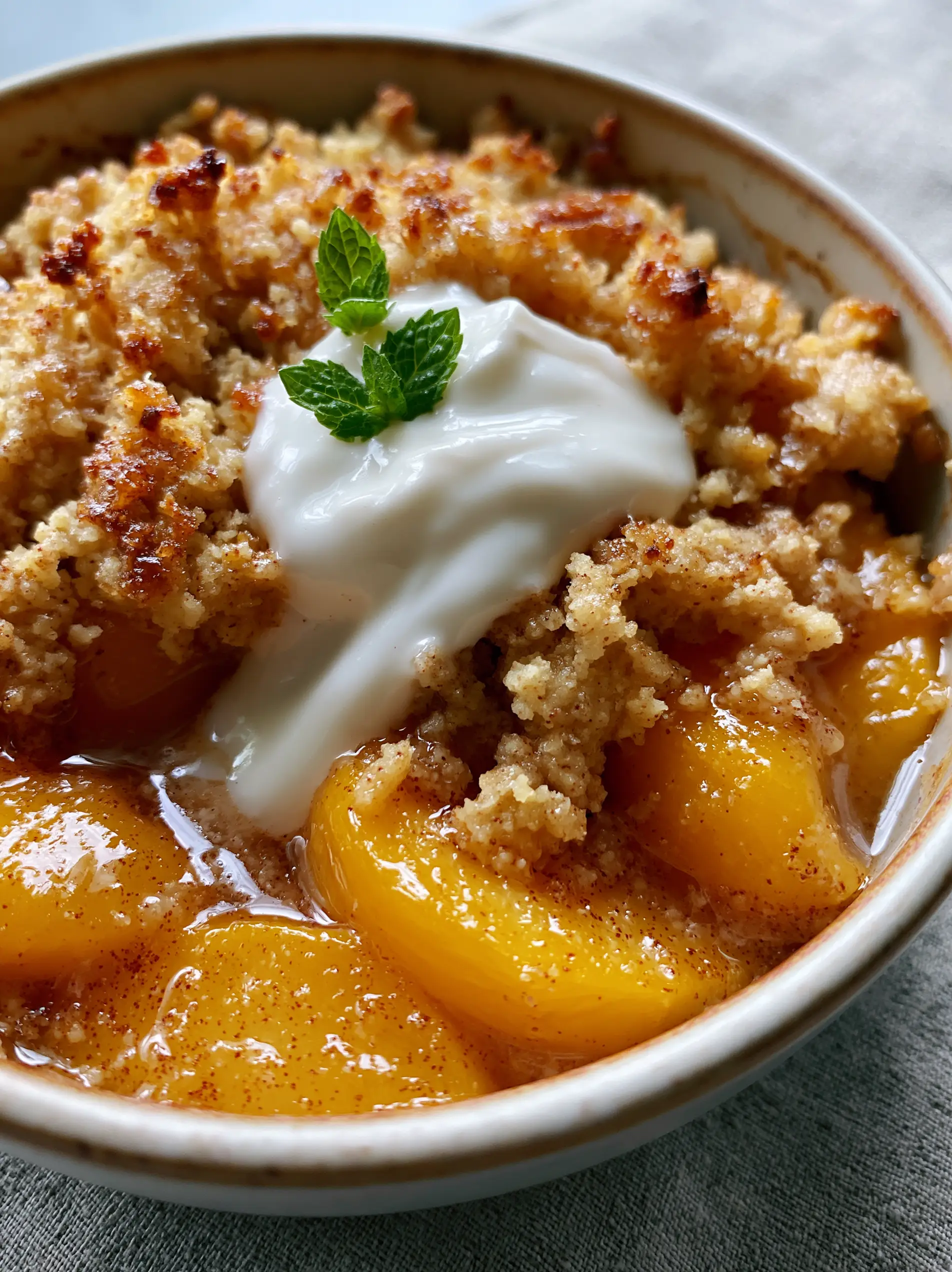 Macro 3/4 angle shot of Paleo Peach Cobbler showing vibrant orange peaches and glistening cinnamon-flecked syrup. (Paleo Peach Cobbler)