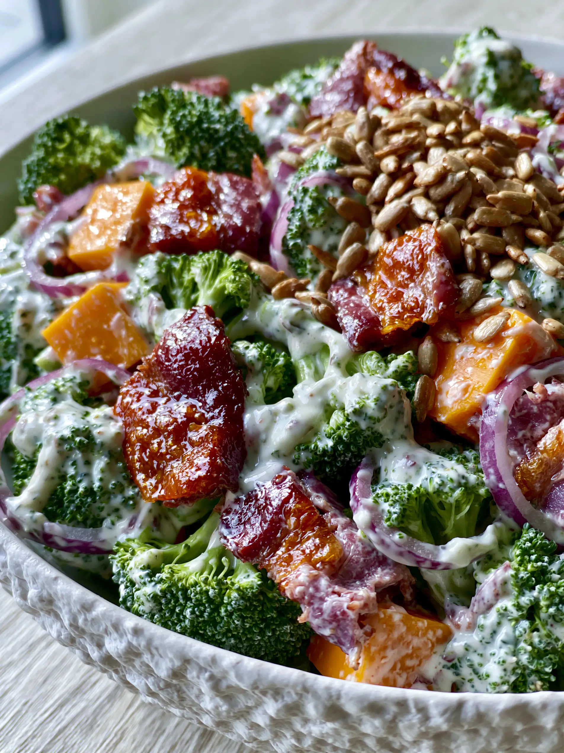 Extreme close-up of cold broccoli salad showing glossy dressing pooling in broccoli crevices and glistening bacon.