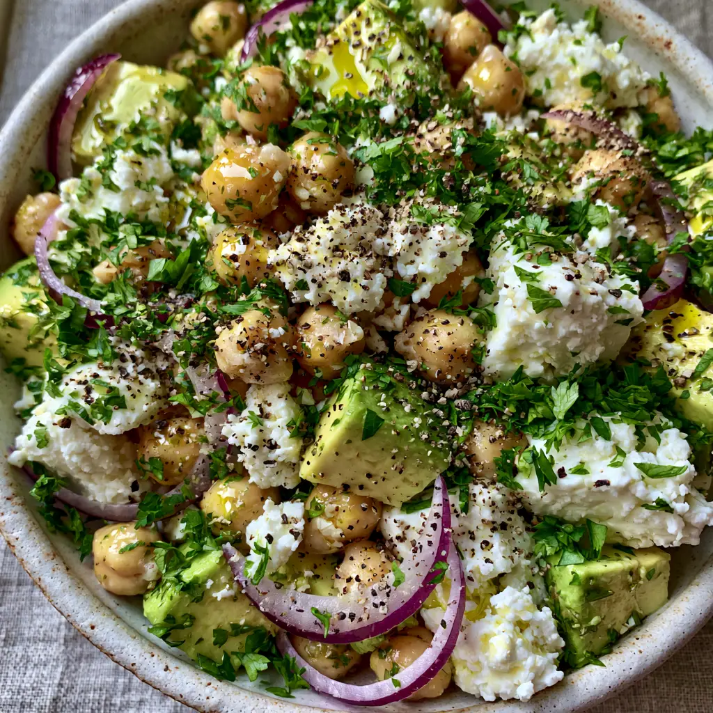 Macro close-up of a chickpea feta avocado salad featuring golden-tan chickpeas, feta crumbles, and red onion crescents. (chickpea feta avocado salad)