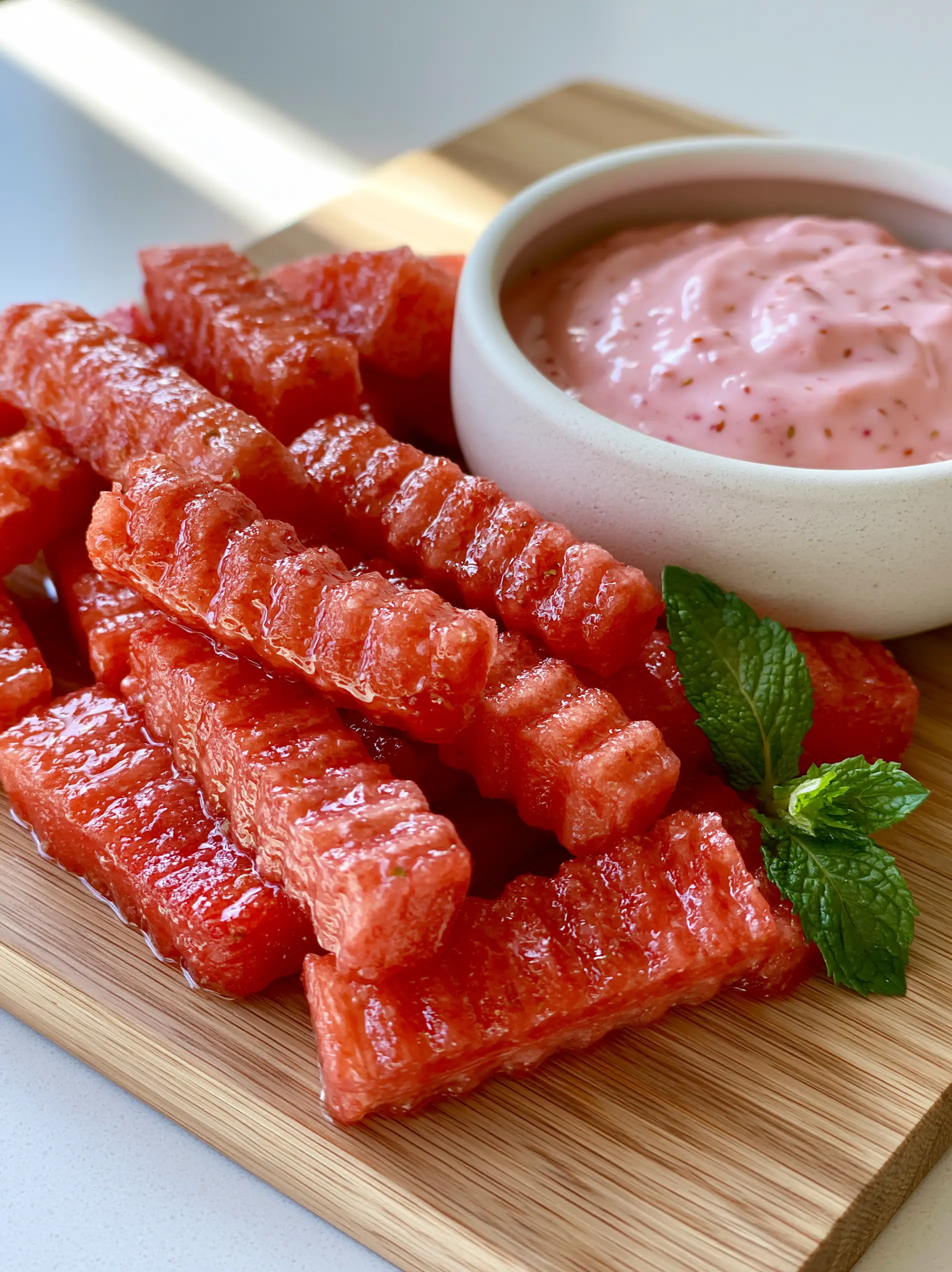 Close up shot of Watermelon Fries with glistening condensation and deep ridges next to a pink yogurt dip.