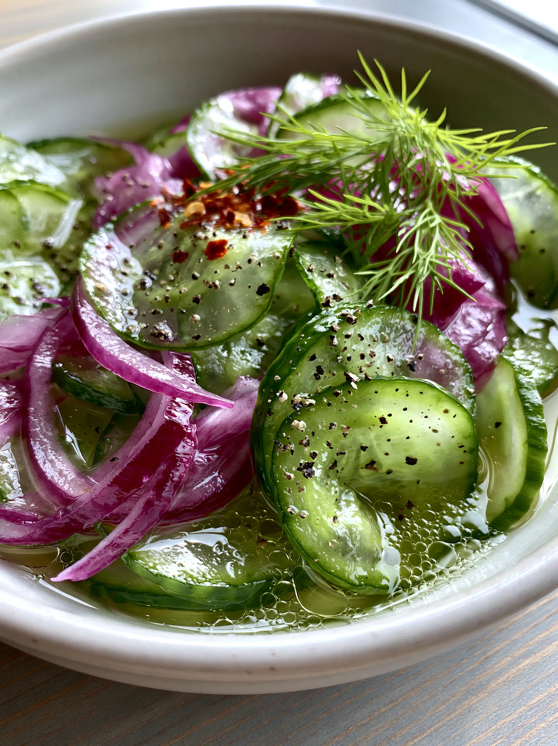 Close-up smartphone photo of translucent emerald cucumber slices and purple onion slivers in clear brine. (Cucumbers and onions in vinegar)