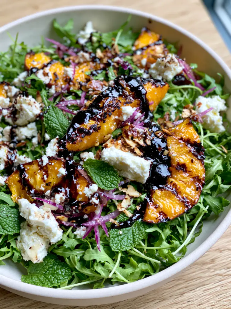 Close-up of toasted almonds and purple onion slivers on a fresh peach feta salad.