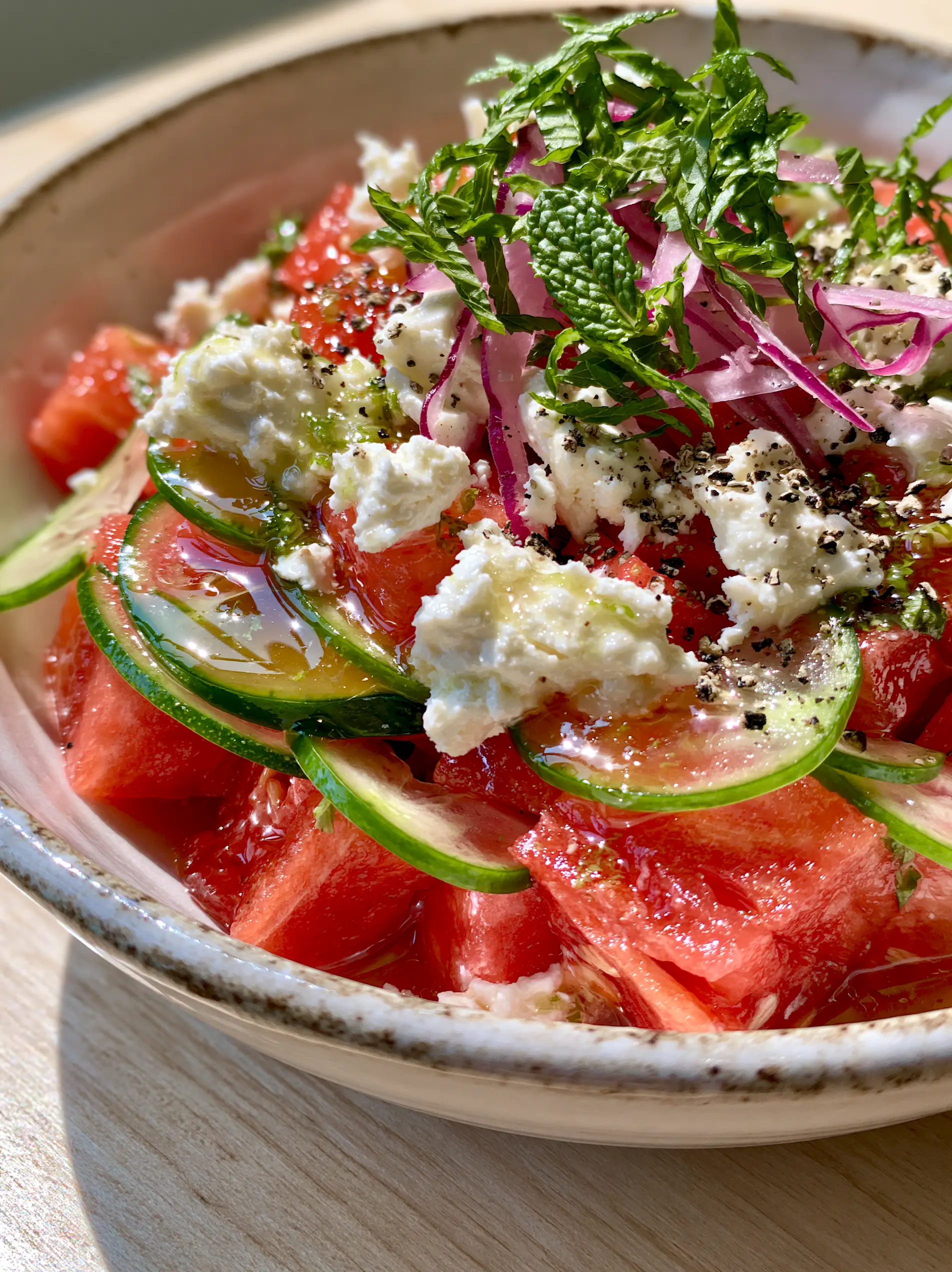 Top-down view of Watermelon Cucumber Feta Salad with glossy lime dressing and fresh julienned mint leaves.