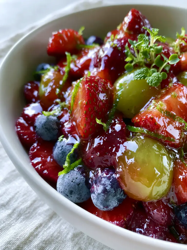 Close up of halved green grapes and strawberry quarters in a honey lime fruit salad with lime zest ribbons.